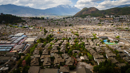 Aerial view of Lijiang Old Town, Yunnan, China. Traditional wooden rooftops and narrow streets surrounded by mountains in a historic UNESCO heritage city