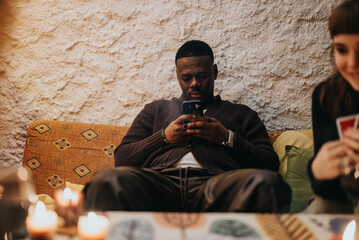 A man relaxes seated indoors, engaged with his smart phone, surrounded by minor details of other...