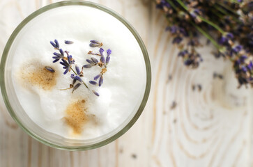 Large glass of hot Lavender Latte on a white wooden table with flowers in the background. Concept of high-quality coffee drinks. Horizontal orientation. Selective focus. Copy space. Top view