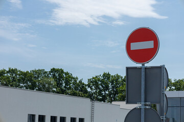 A bright red do not enter sign stands prominently in front of modern buildings under a blue sky,...