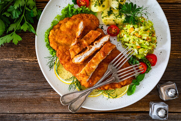 Crispy breaded chicken cutlets with boiled potatoes and young cabbage salad on wooden table	