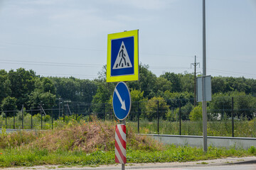 Two traffic signs stand prominently beside a road, signaling a construction zone and directing...
