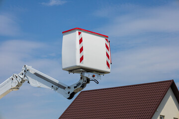 A worker operates an elevated platform to perform maintenance tasks on a residential roof in bright...