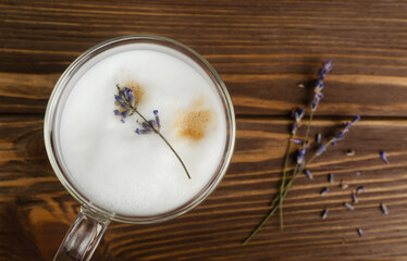Large glass of hot Lavender Latte on a brown wooden table with flowers in the background. Concept of high-quality coffee drinks. Horizontal orientation. Selective focus. Copy space. Top view