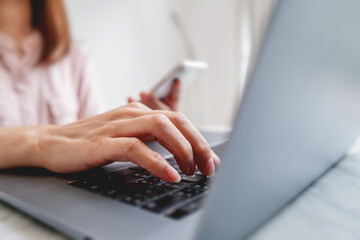 Businesswoman using laptop computer with smartphone working and surfing the internet to search for information.