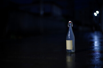Empty Glass Bottle with Label on Wet Street at Night