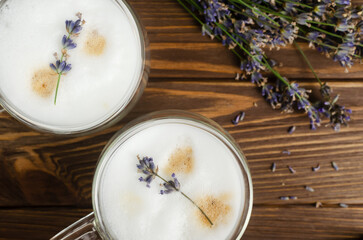 Two cups of hot lavender latte on a white wooden table with flowers in the background. Concept of high-quality coffee drinks. Horizontal orientation. Selective focus. Copy space. Top view