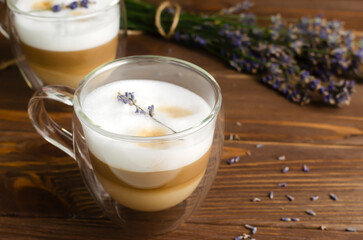 Two cups of hot lavender latte on a white wooden table with flowers in the background. Concept of high-quality coffee drinks. Horizontal orientation. Selective focus. Copy space.