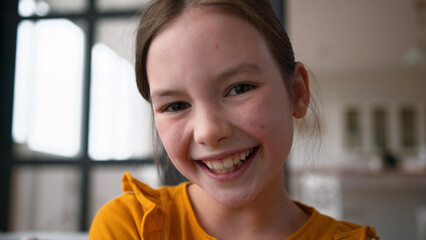 Joyful Caucasian child portrait schoolgirl girl close up looking at camera posing. Happy kid little...