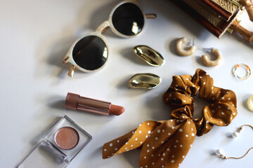 Wicker purse, sunglasses, scrunchie, lipstick and various gold and neutral jewelry on white background. Selective focus.