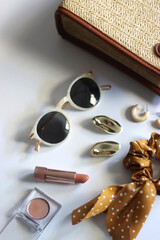 Wicker purse, sunglasses, scrunchie, lipstick and various gold and neutral jewelry on white background. Selective focus.