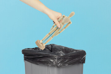 Throw wooden man, in the trash, outstretched hand with wooden mannequin in front of trash can