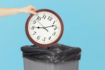 Throw round wall clock in the trash, outstretched hand with round wall clock in front of trash can
