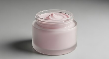 A close up shot of a small clear glass jar filled with pink cream on a grey gradient background