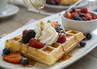 Delicious waffle with fresh berries and whipped cream being drizzled with syrup
