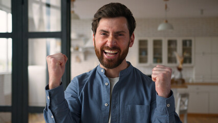 Happy joyful Caucasian guy man winner dad smiling clenching fists male winning rejoicing at home...