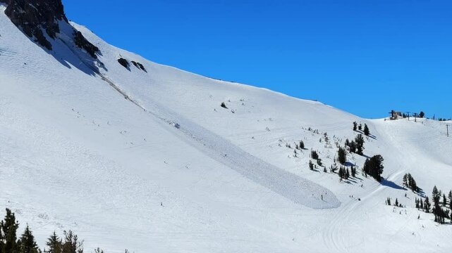 Inbound avalanche run off debris Spring winter sunny blue sky blue bird day main lodge Mammoth Mountain ski resort California aerial drone skiing snowboard groomed trail run spring corn snow pan left