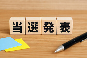 当選発表の文字が書かれた木製ブロックと黒いペンの構図