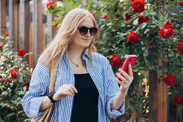 A portrait of a smiling beautiful 30s woman texting with her phone. Summer time. Young female in casual clothing standing outdoor