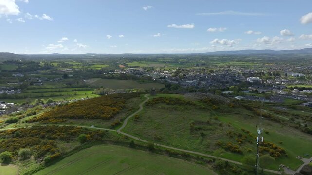 Vinegar Hill, Enniscorthy, County Wexford, Ireland, April 2025. Drone orbit and tilt down as cloud shadow crosses over top of grassy hill monument with dense town in distance.
