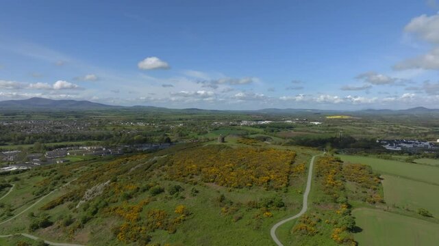 Vinegar Hill, Enniscorthy, County Wexford, Ireland, April 2025. Drone slow gradual approach from far away keeping stone rock tower monument at center above cliff and dense shrub vegetation.