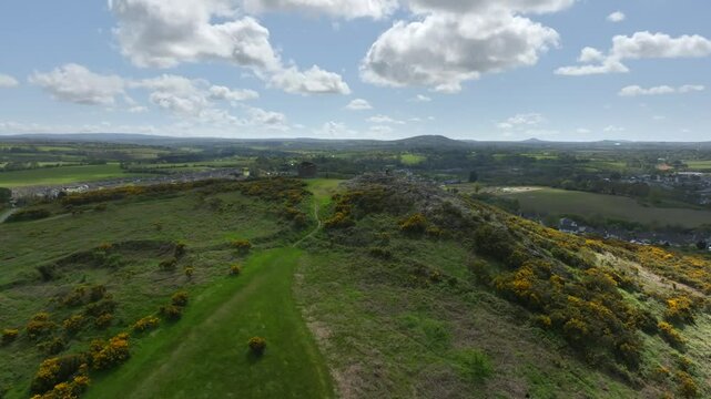 Vinegar Hill, Enniscorthy, County Wexford, Ireland, April 2025. Drone tilt up with medium establishing orbit counter clockwise as sunlight breaks and shines between clouds illuminating lush greens.