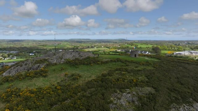 Vinegar Hill, Enniscorthy, County Wexford, Ireland, April 2025. Drone establishing orbit from rocky cliff with people sitting and admiring view to ascend above walking path to stone tower monument.