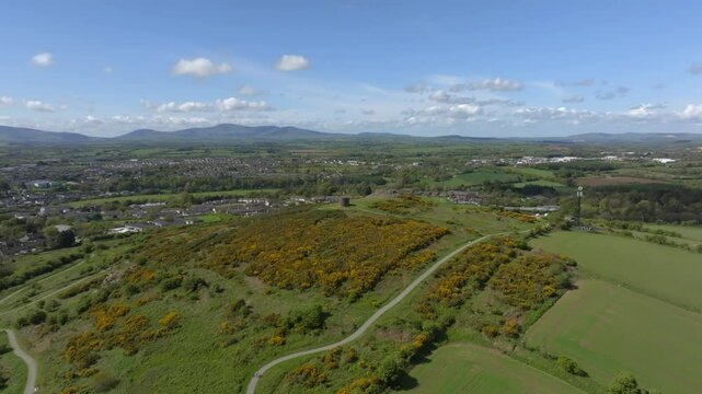 Vinegar Hill, Enniscorthy, County Wexford, Ireland, April 2025. Drone panoramic aerial establishing pullback gradually reveals hiking paths through low scrub vegetation and nearby town buildings.