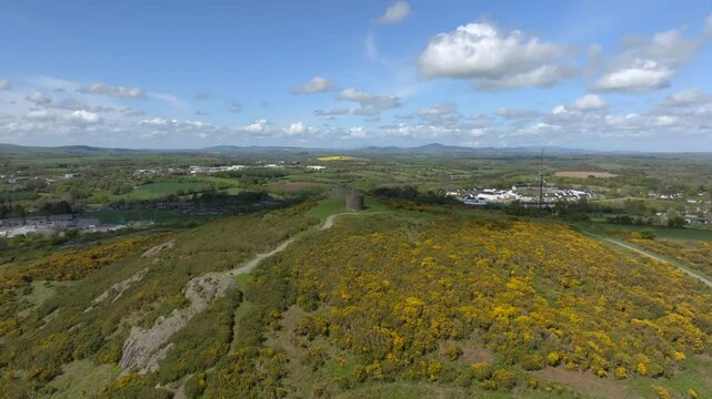 Vinegar Hill, Enniscorthy, County Wexford, Ireland, April 2025. Drone stunning panoramic establishing pullback showcases rocky cliff band rising to tower monument and low dense shrub vegetation.