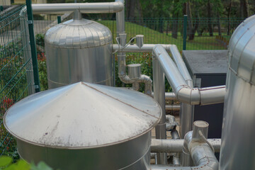 Stainless steel pipes and tanks at a water treatment or pumping station next to a green fence and...