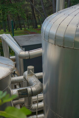 Stainless steel pipes and tanks at a water treatment or pumping station next to a green fence and...