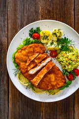 Crispy breaded chicken cutlets with boiled potatoes and young cabbage salad on wooden table	