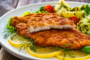 Crispy breaded chicken cutlets with boiled potatoes and young cabbage salad on wooden table	