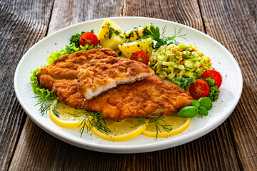 Crispy breaded chicken cutlets with boiled potatoes and young cabbage salad on wooden table	