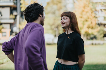 A cheerful young couple converses in a sunlit park setting, showcasing happiness and connection....