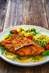 Crispy breaded chicken cutlets with boiled potatoes and young cabbage salad on wooden table	