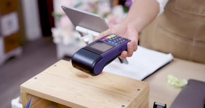Credit card being inserted into POS terminal during cashless transaction in flower shop operated by Asian elderly florist running successful small business after retirement