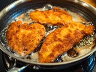 Frying crispy breaded chicken cutlets in frying pan, close-up