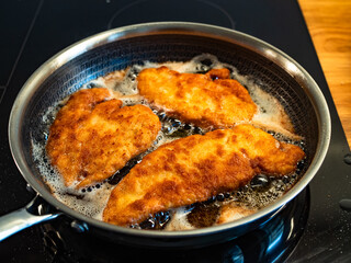 Frying crispy breaded chicken cutlets in frying pan, close-up