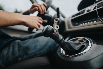 A close-up view of a manual gear shift with a driver's hands on the steering wheel, highlighting...