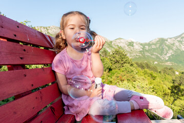 Cute funny little girl toddler child blowing soap bubbles in park summer outside