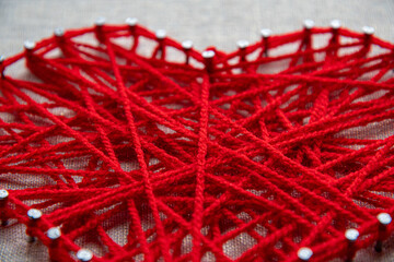 Colorful and intricate string art displays a heart shape formed by intertwined red yarn wrapped...
