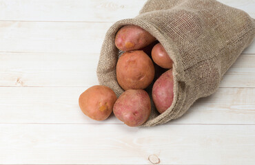 Red, raw potatoes in jute bag on wooden background