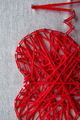 Colorful string art display showcases heart shape meticulously crafted from red yarn and nails.