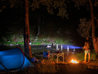 Night at the campsite. A man with a flashlight in his hand illuminates the stone totems in the...