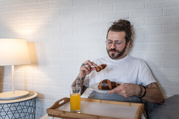 Man enjoying breakfast in bed with croissant and orange juice