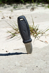 The hunting knife with a black handle is stuck in the sand