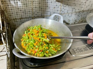 housewife is cooking stir-fried tempeh, green beans and carrots using a frying pan and spatula on the stove, a dish suitable for serving as breakfast