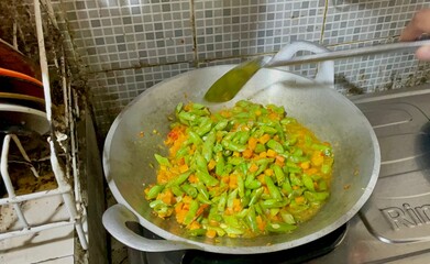 housewife is cooking stir-fried tempeh, green beans and carrots using a frying pan and spatula on the stove, a dish suitable for serving as breakfast