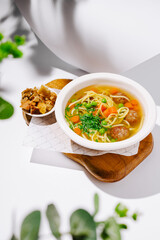 Warm bowl of flavorful soup with meatballs and vegetables on a wooden tray